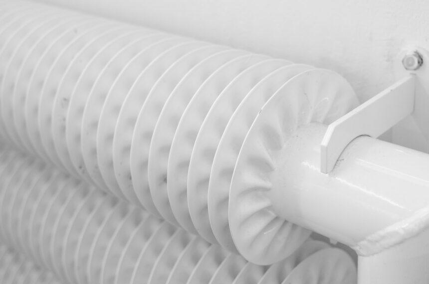 White metal tubed radiator system with pipe for industrial heating mounted to wall with hook in light room at home