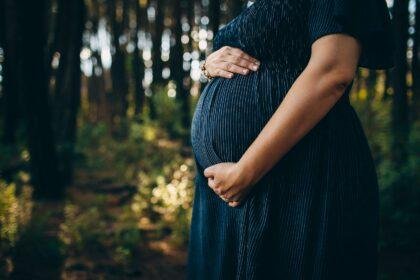 Pregnant woman embracing belly while standing in forest