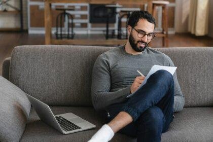 Arabian Man check bills bank account balance statement remote e-payment through e-bank app on laptop