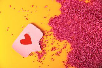 Red like heart icon on a pink pin next to pink balls texture.