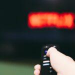 Woman using remote control to switch streaming service on television